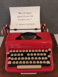 A typewriter with a sheet of paper inserted. On the paper: the line, "'Write what should not be forgotten.—Isabel Allende.'"