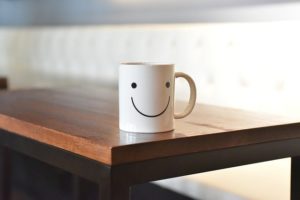 Cup of coffee (decorated with a smiley face) on a table.
