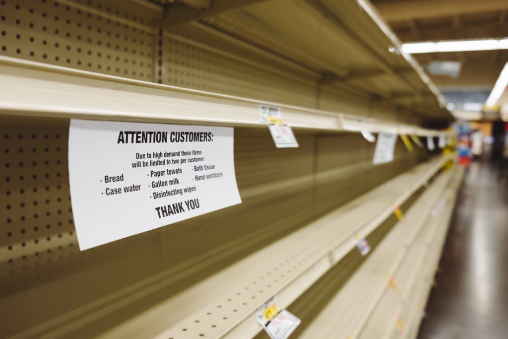 Empty supermarket shelves with a notice about limited-purchase policies for certain items.